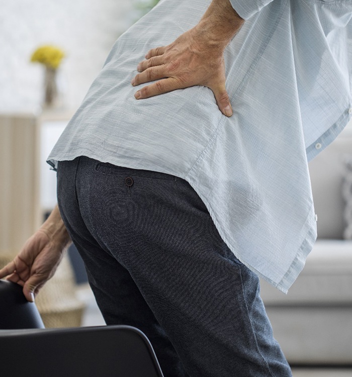 older man holding back while getting out of chair