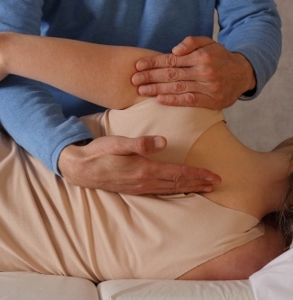Doctor using osteopathic manipulative treatment on patient with shoulder pain