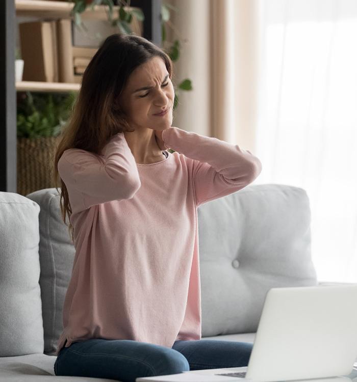 woman experiencing neck pain while using laptop on couch 