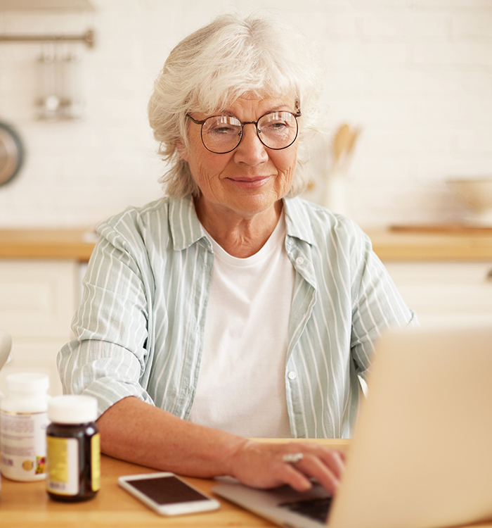 Older woman on her laptop with bottles of nutritional supplements